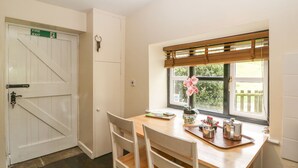 A dining area with a wooden table, white chairs, a window with a view of greenery, and a fire exit sign. - Aqueduct Cottage (Pontypool)