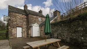 A stone building with a white door, a small shed, and a picnic table with a green umbrella. - Aqueduct Cottage (Pontypool)