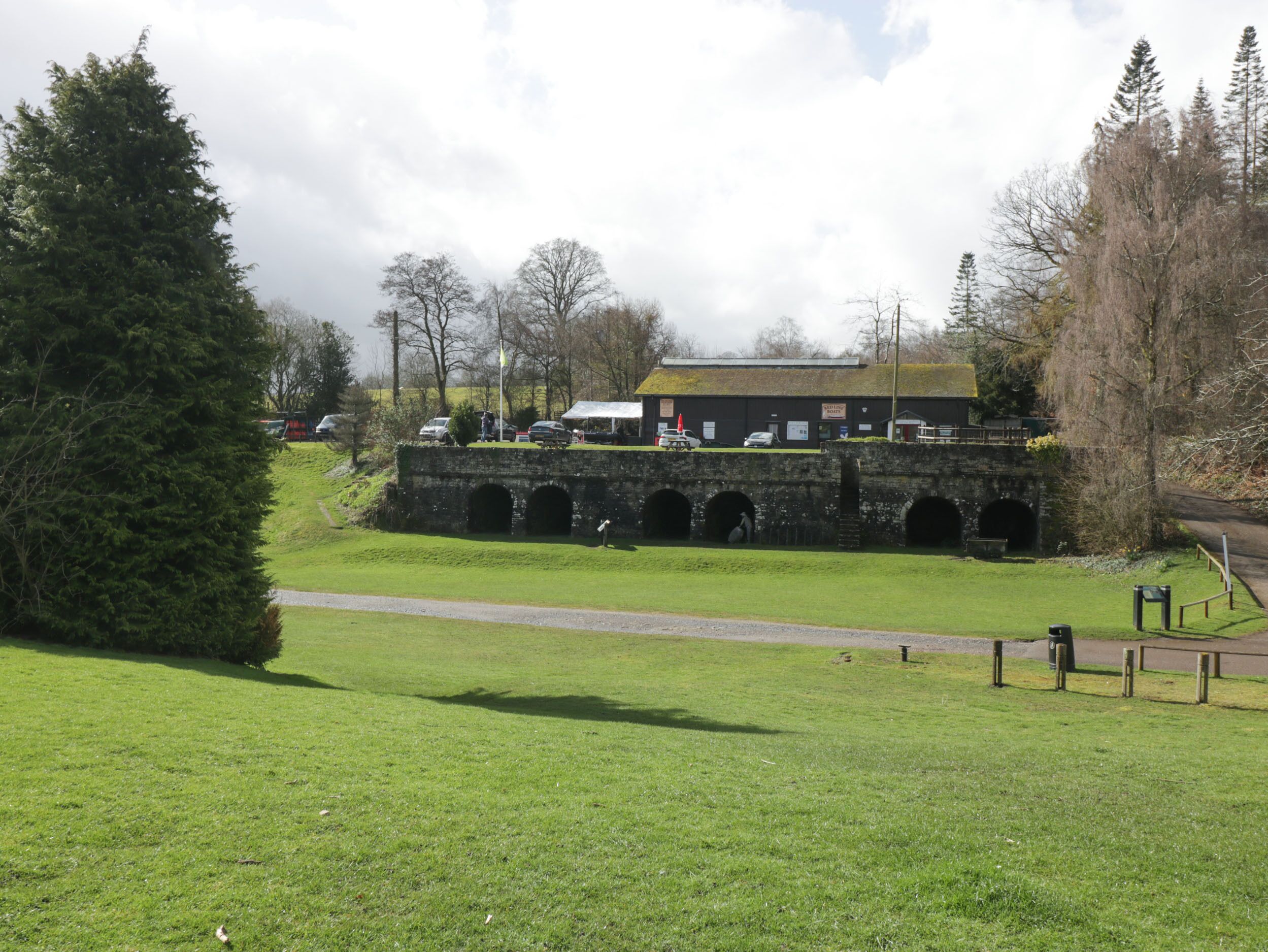 Uma ponte de pedra com várias arcadas, uma área gramada em primeiro plano e um edifício com uma placa que diz 'WATERINGHOUSE'.