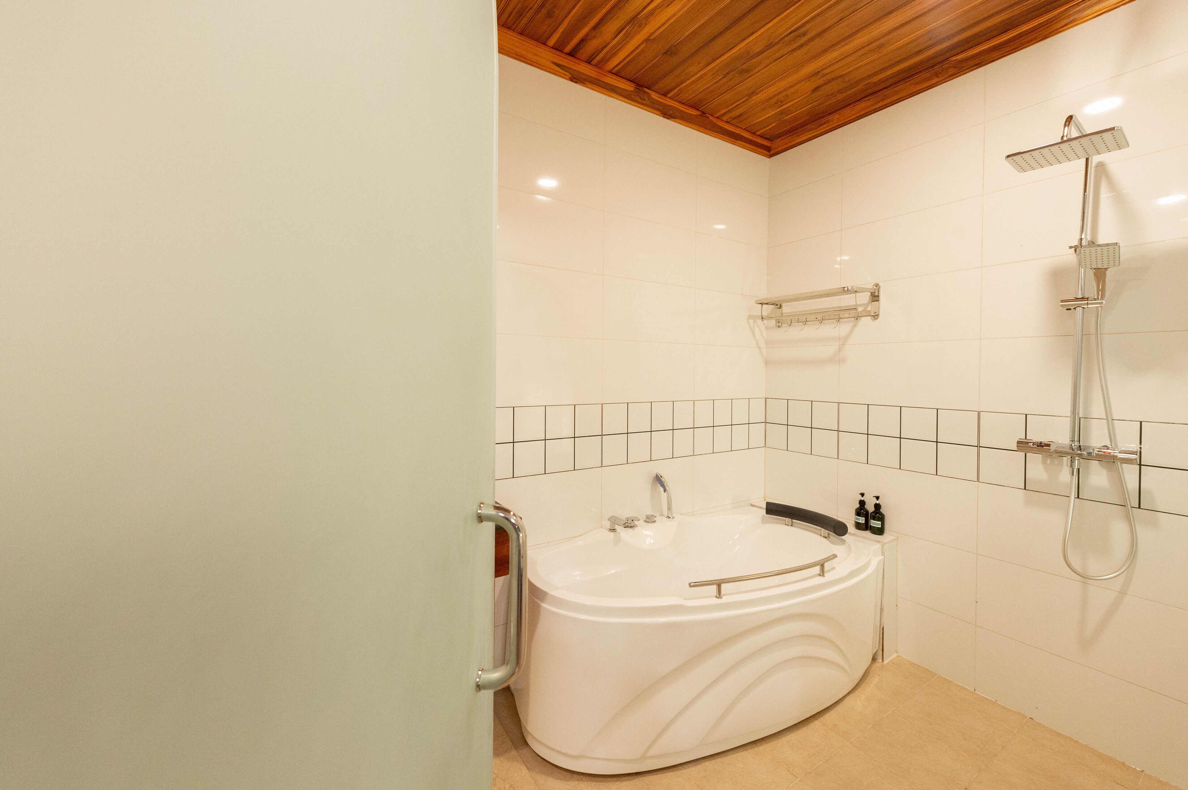 A bathroom with a white bathtub, a shower, and a wooden ceiling.