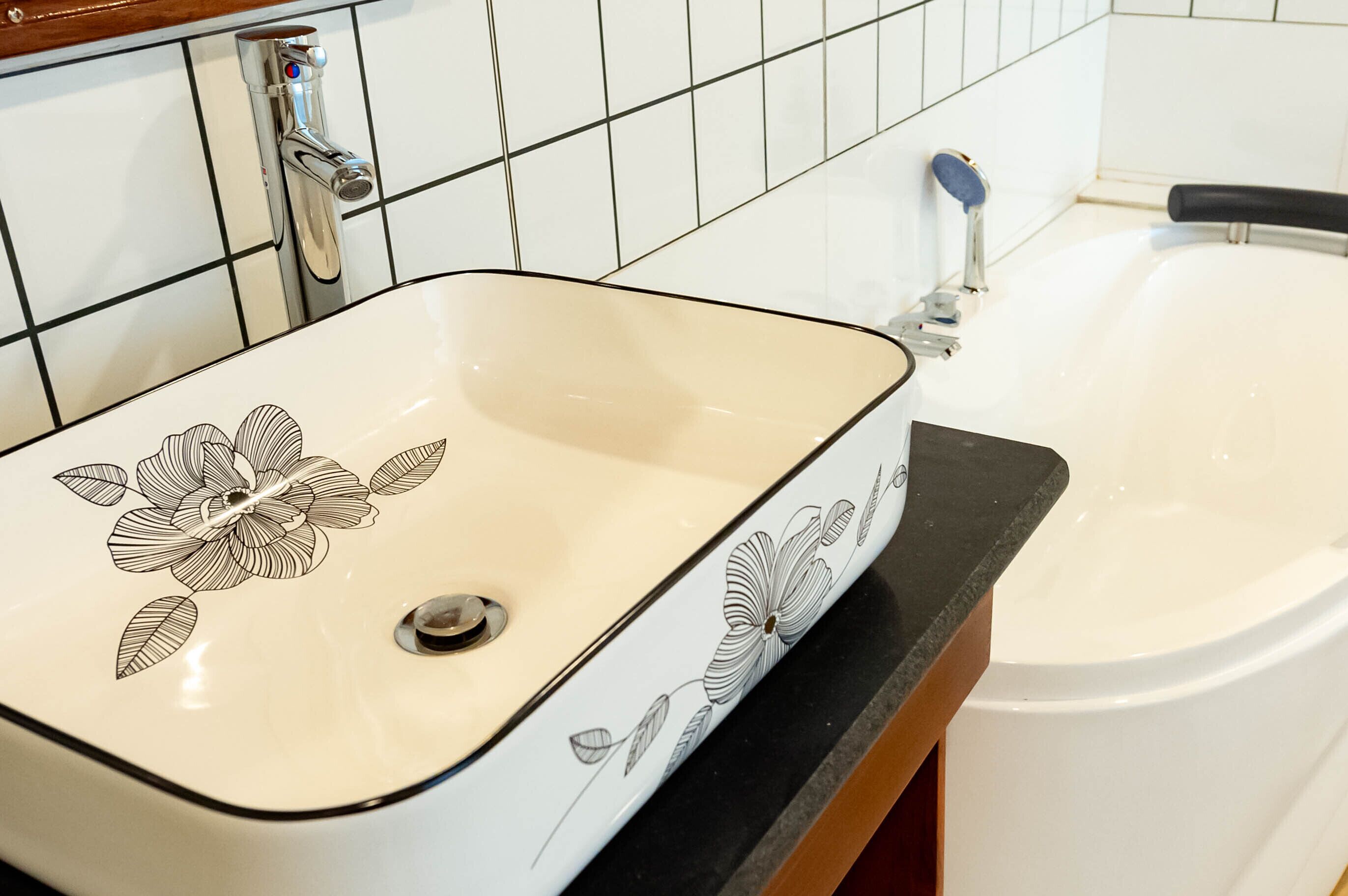 Une salle de bain avec un lavabo blanc orné d’un motif floral et une baignoire.