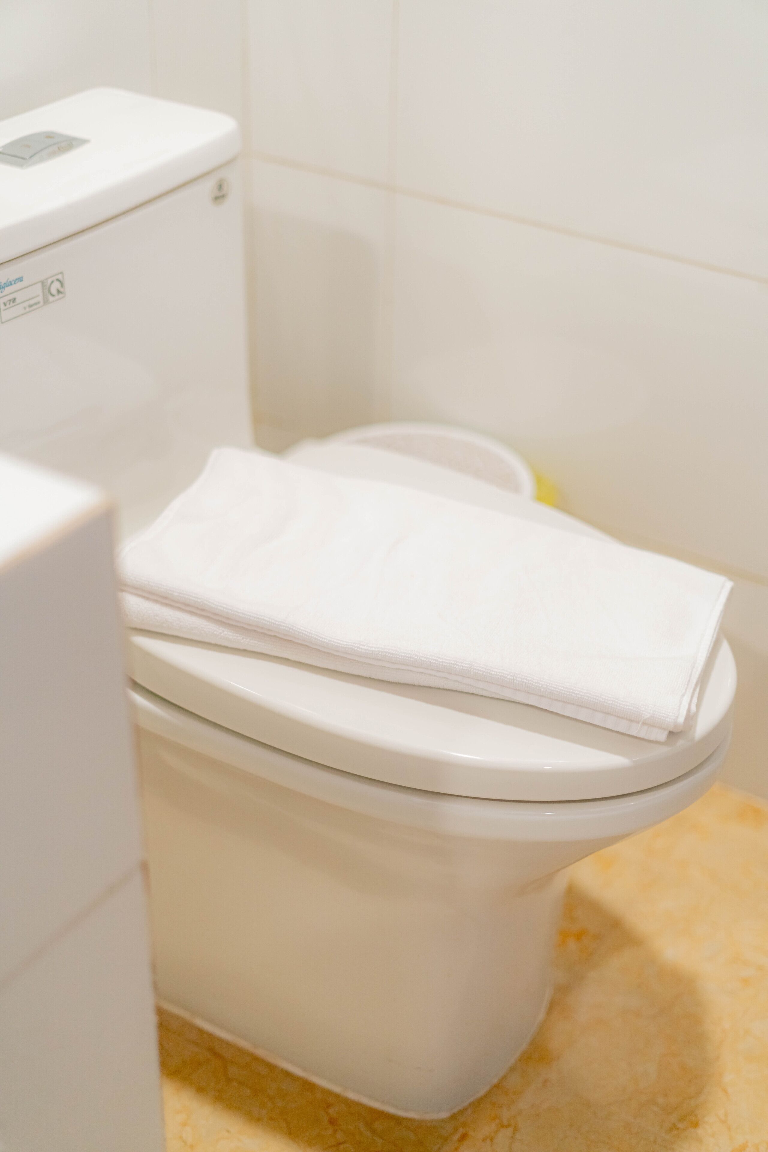Des toilettes blanches, sur lesquelles est posée une serviette blanche pliée, un panneau de commande visible et un sol de couleur beige.