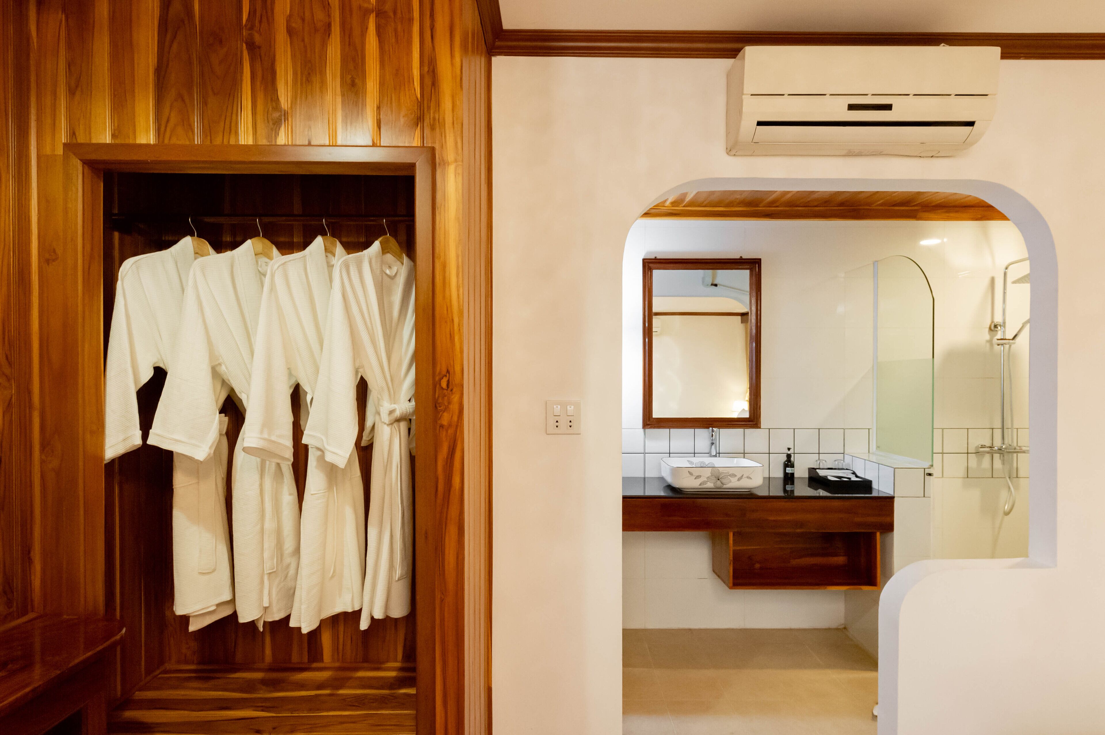A wooden walk-in closet with hanging robes, a bathroom with a wooden vanity, a sink, and a shower.