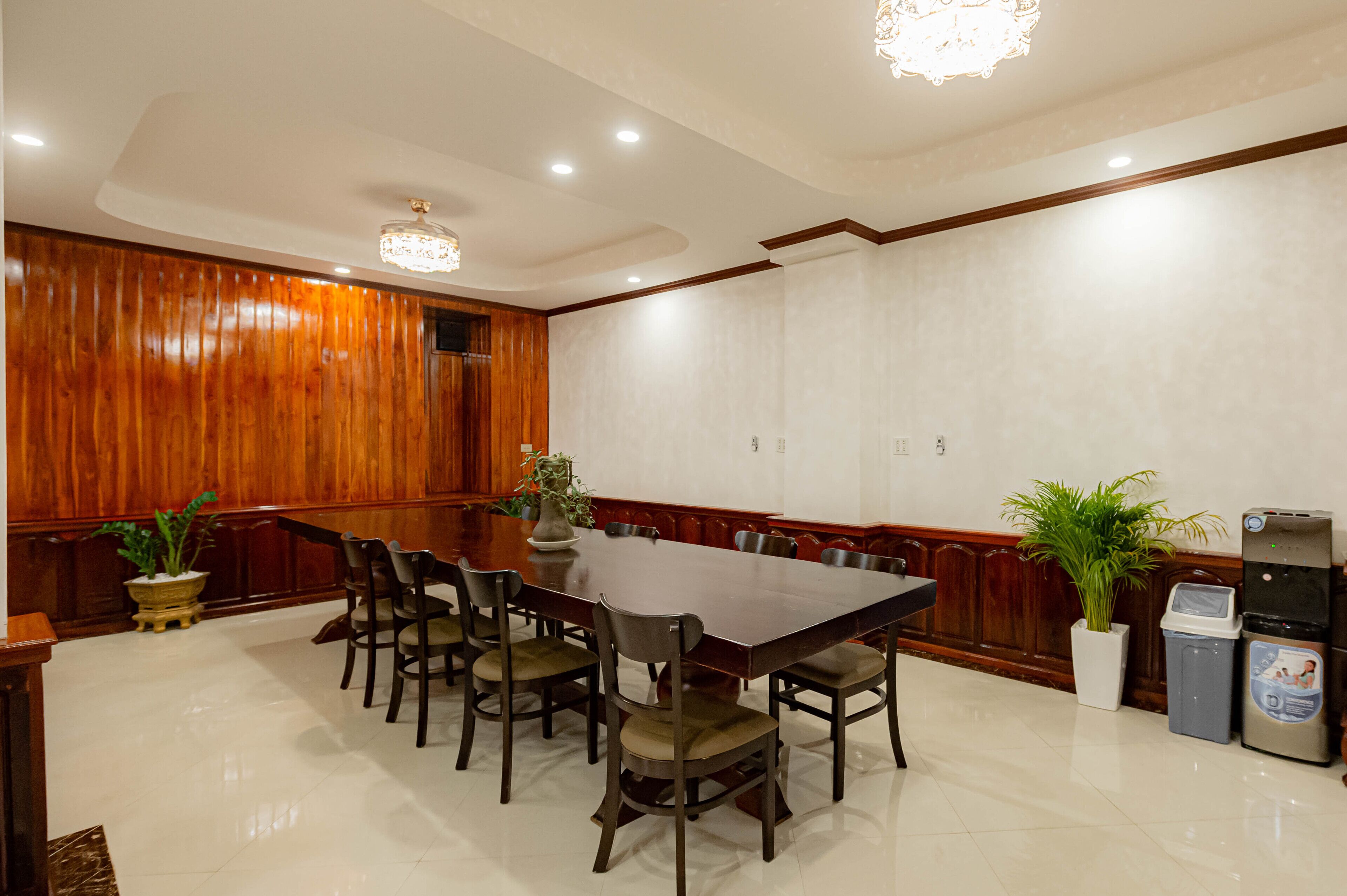 A conference room with a large wooden table, multiple chairs, and potted plants.