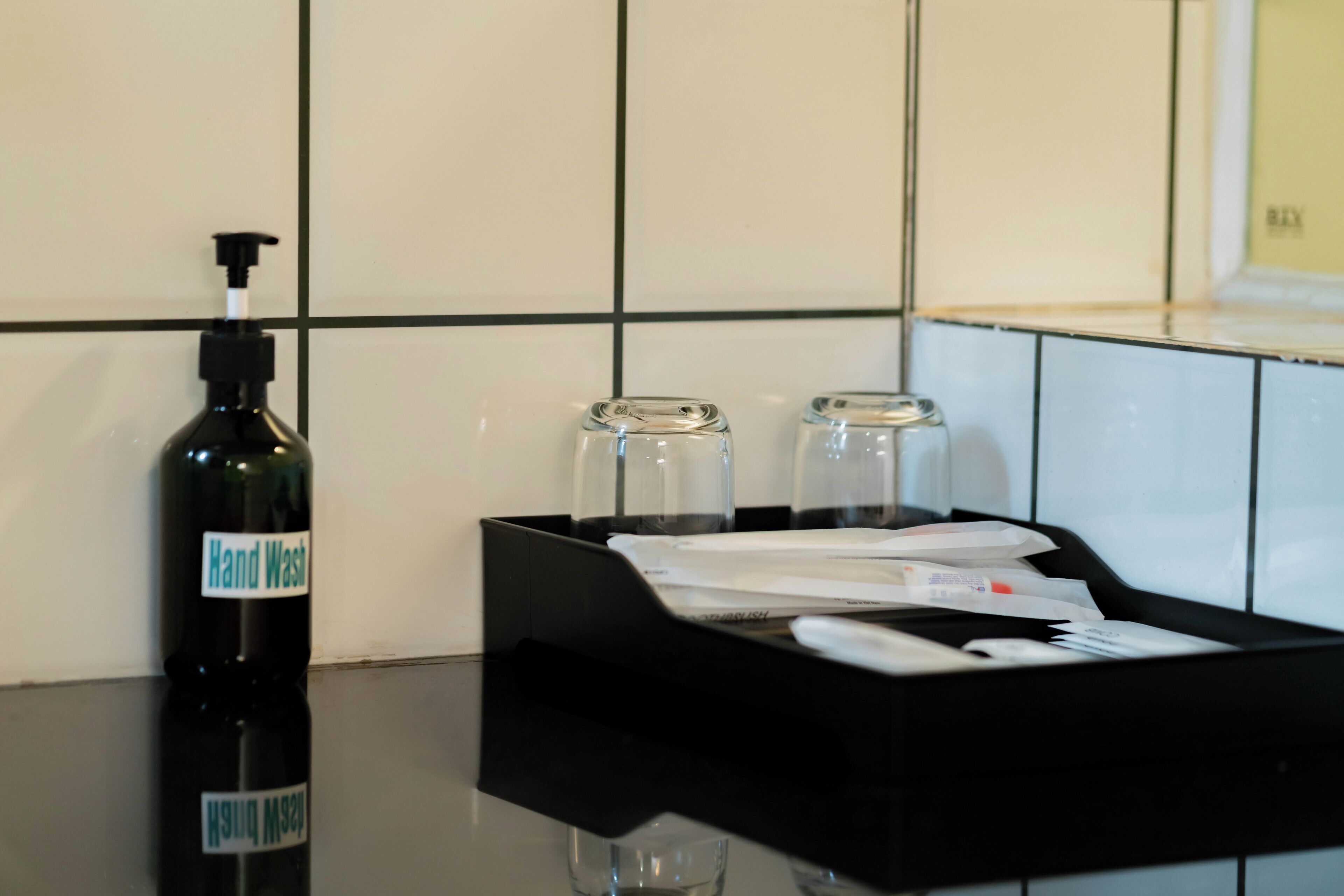 Un flacon de gel hydroalcoolique, deux bouteilles en verre et un plateau noir contenant des papiers et un objet blanc, le tout posé sur un comptoir carrelé.