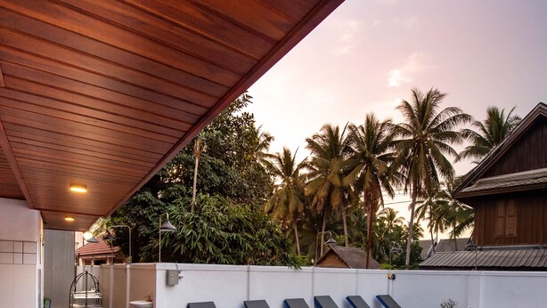 Una piscina infinita con sillas de descanso, techo de madera y vistas a palmeras.