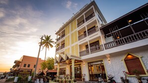 Un hotel de varios pisos con balcones, una entrada principal y plantas en macetas.