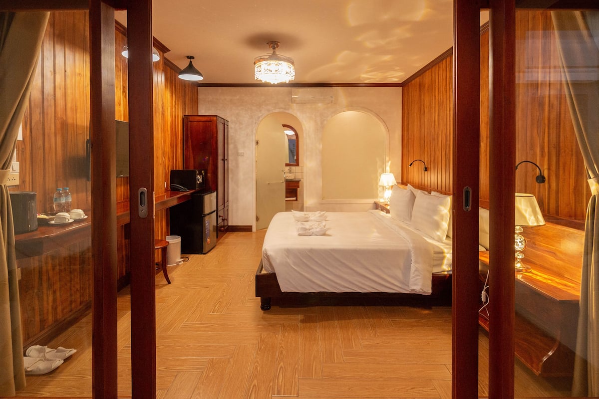 Une chambre d’hôtel avec un plancher en bois, un lit avec du linge de maison blanc, un bureau avec un ordinateur et un miroir.