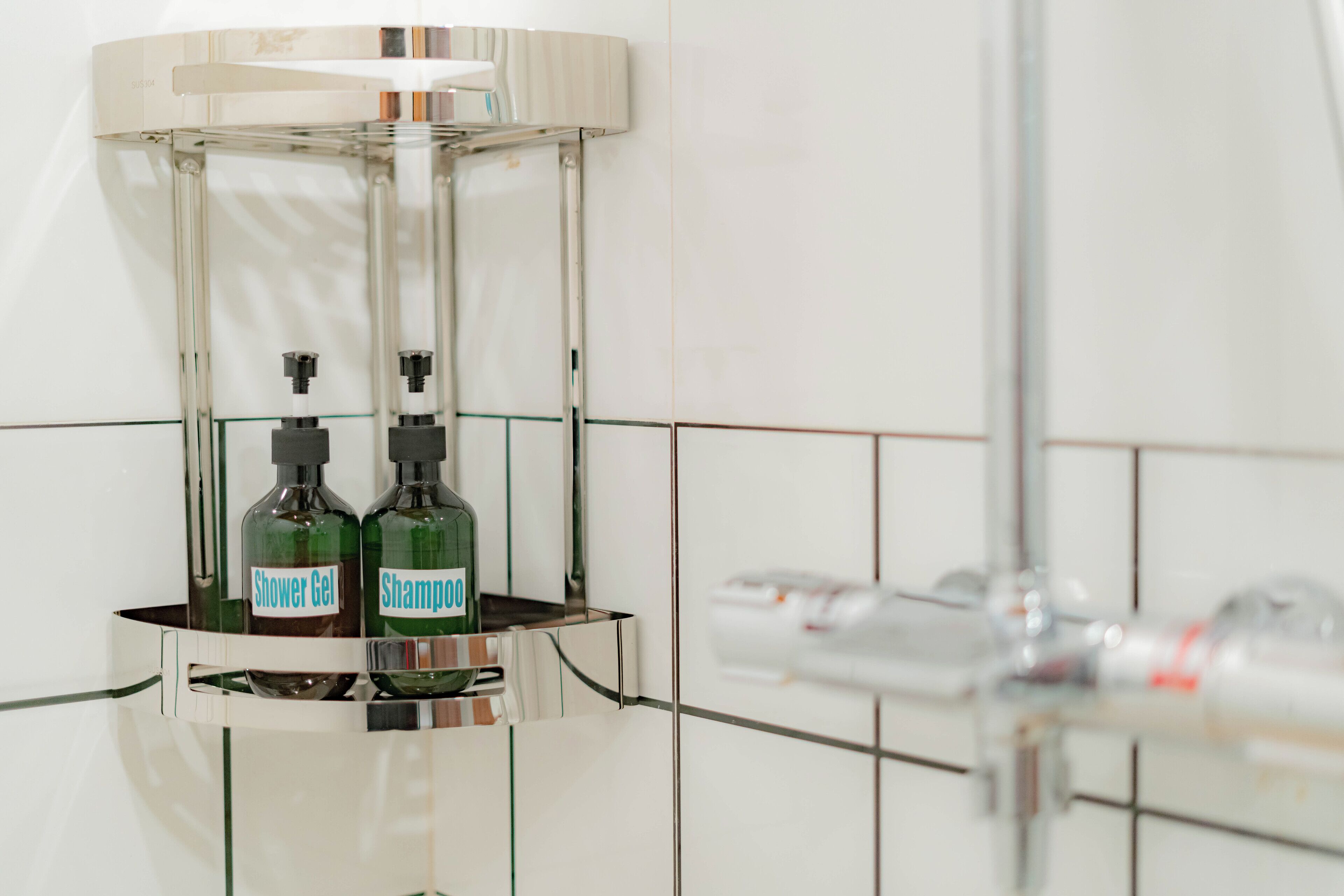 A bathroom with a glass shelf holding two bottles of shower gel and shampoo.