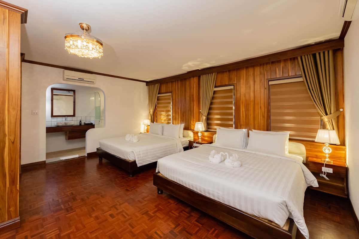 Une chambre d’hôtel avec deux lits, un plancher en bois, un lustre et une salle de bain avec un miroir et un lavabo.