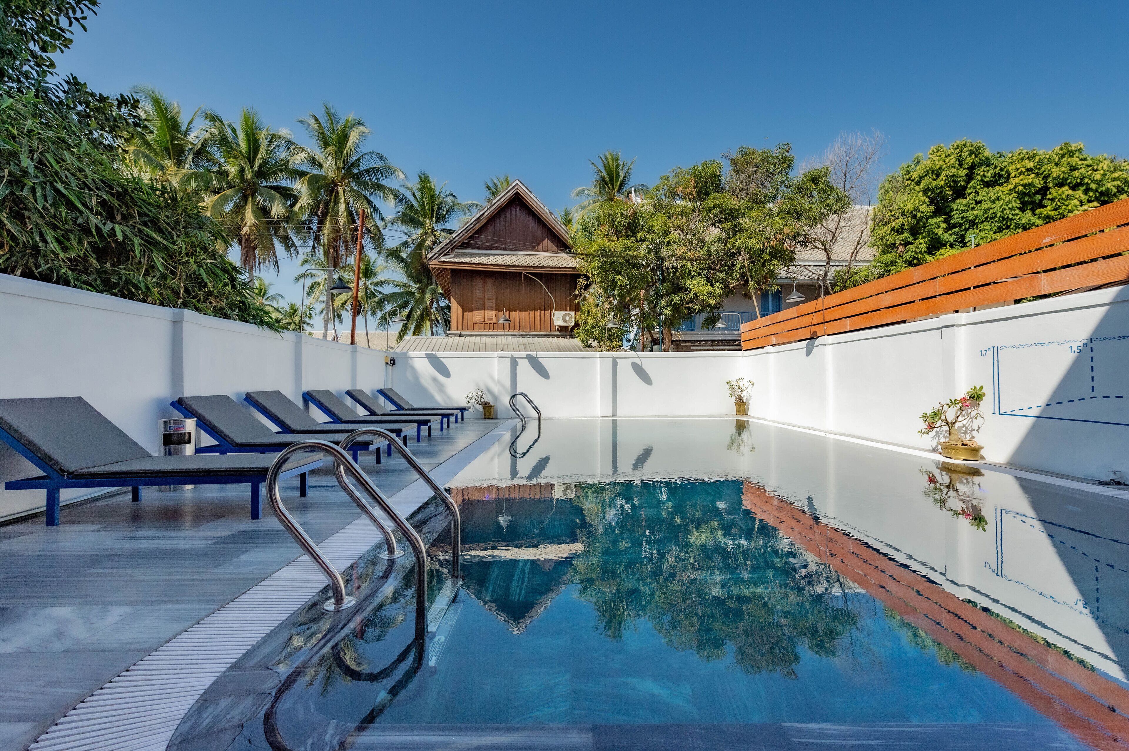 Piscina com espreguiçadeiras e um edifício de madeira ao fundo.
