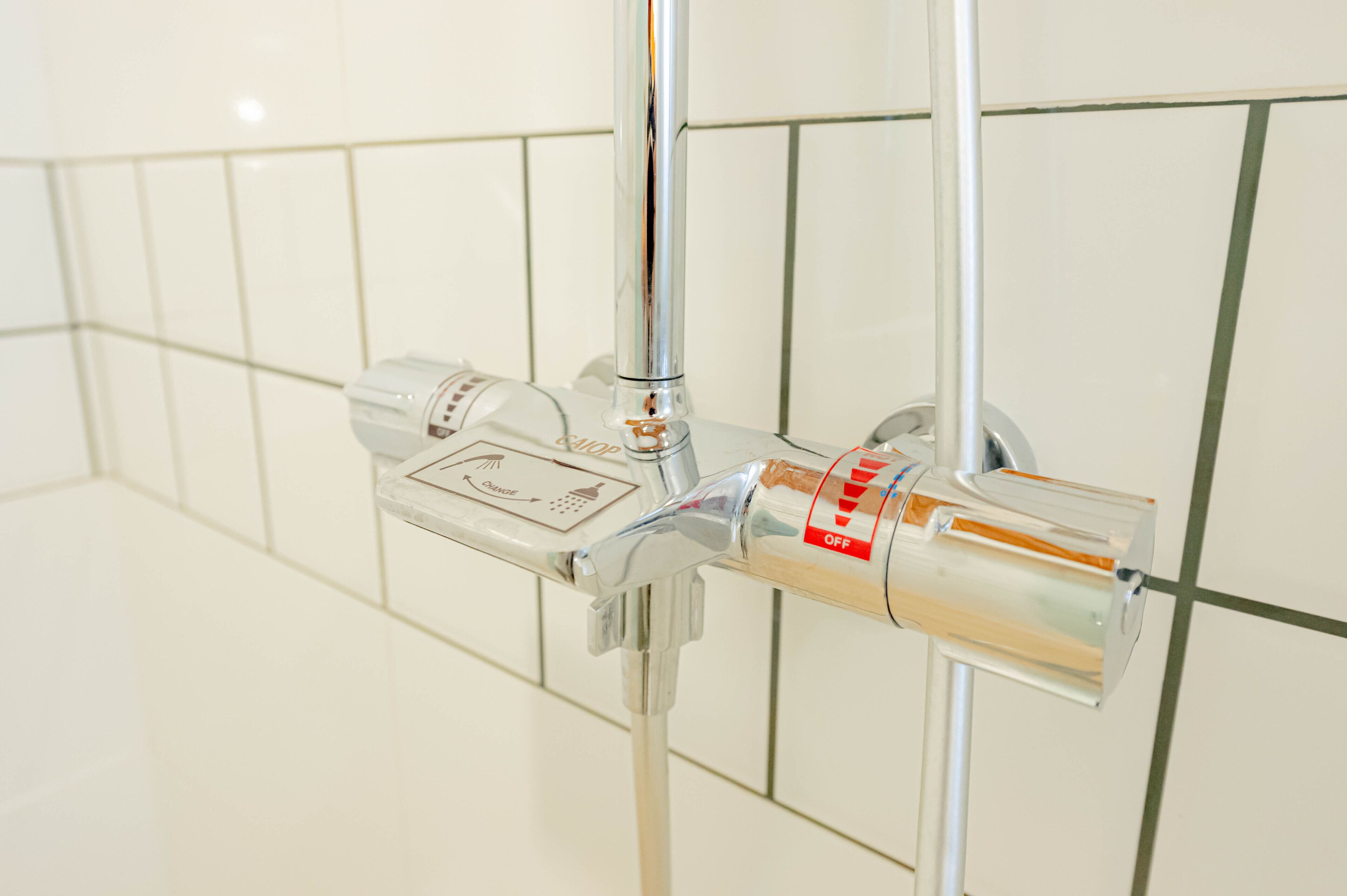 Un control de ducha cromado con dial de temperatura y un interruptor rojo para "OFF".