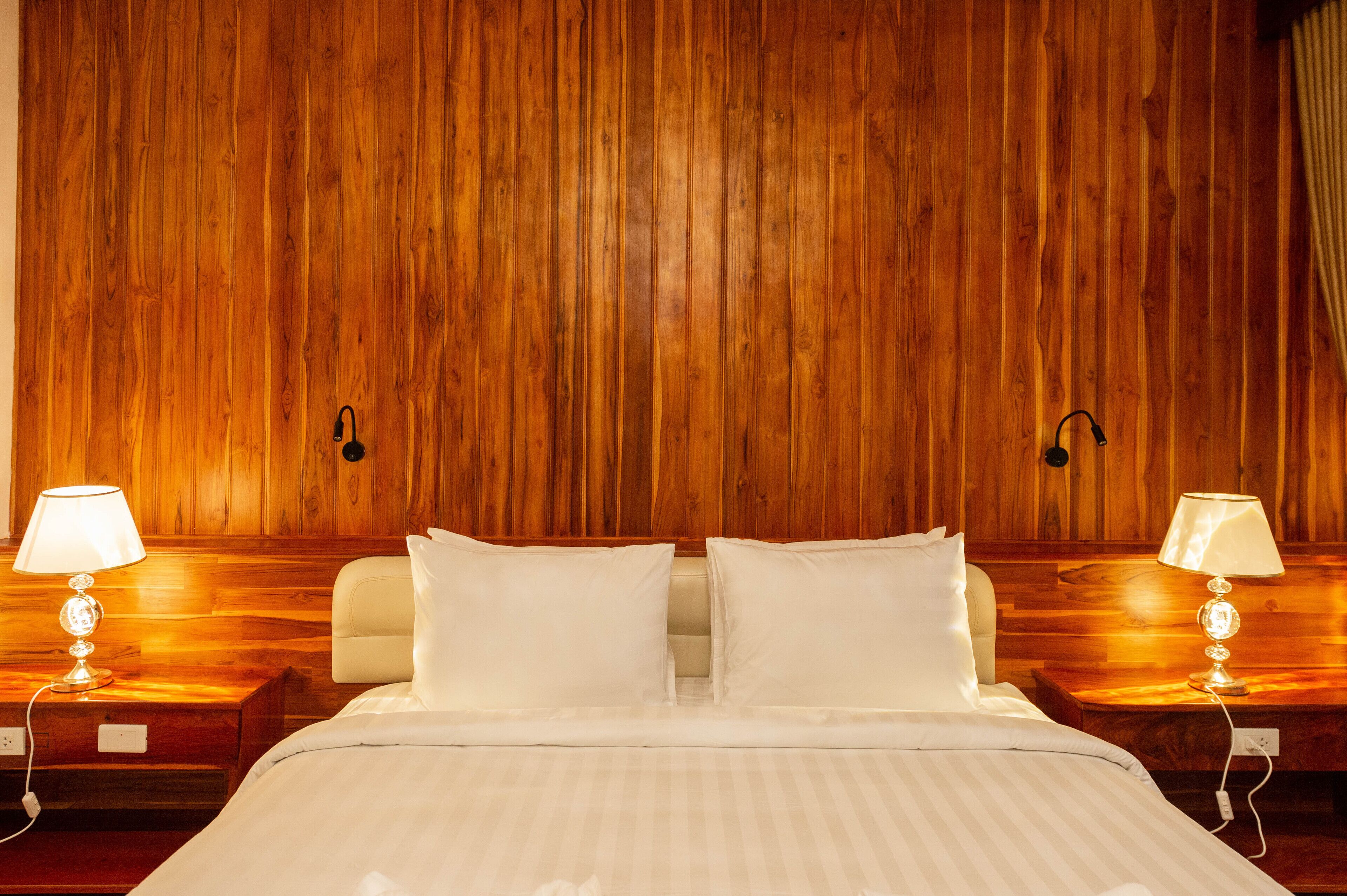 A hotel room with a wooden paneled wall, a bed with white bedding, and two bedside lamps.