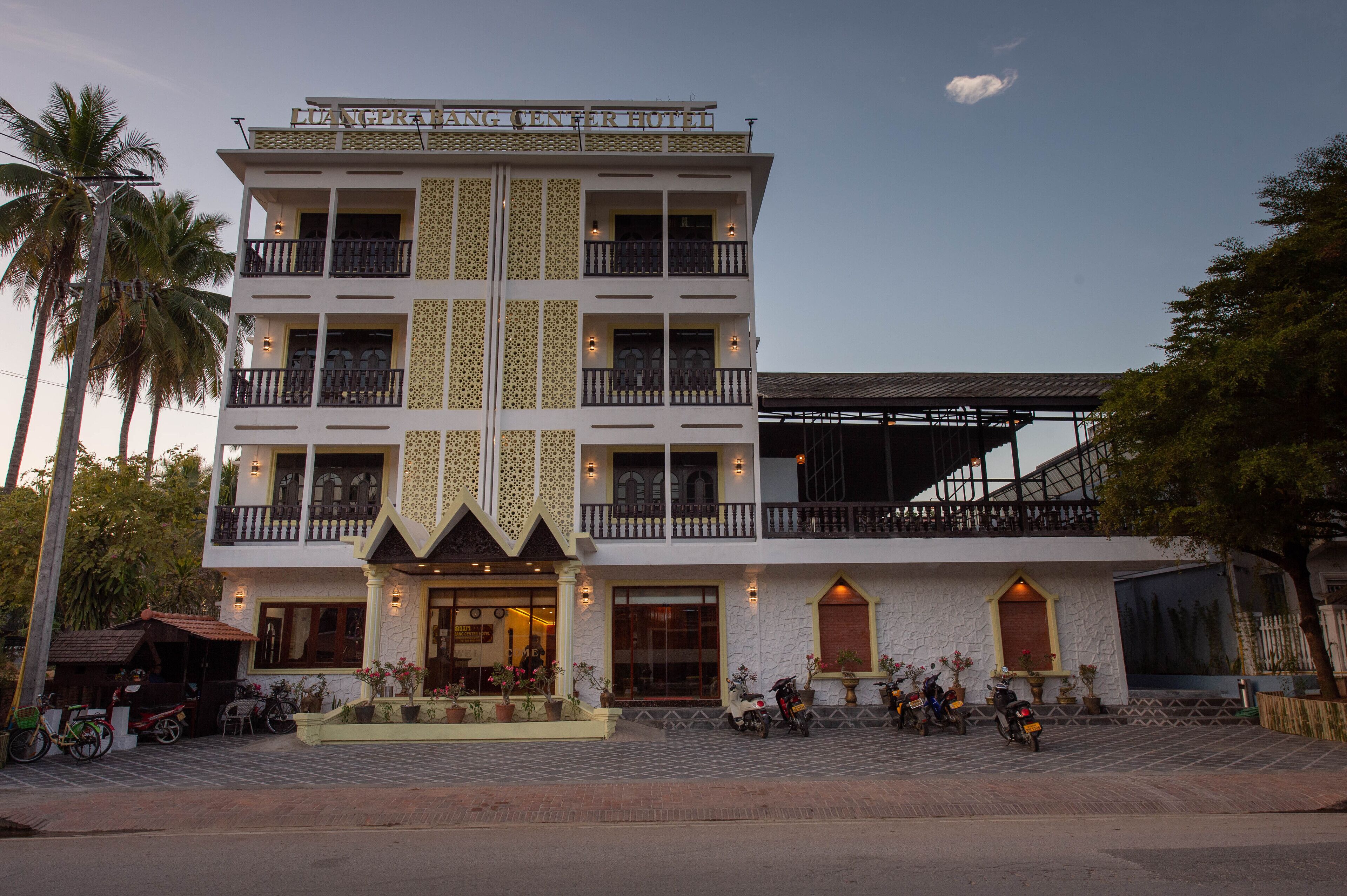 A multi-story hotel with a central entrance, balconies, and a covered outdoor seating area.