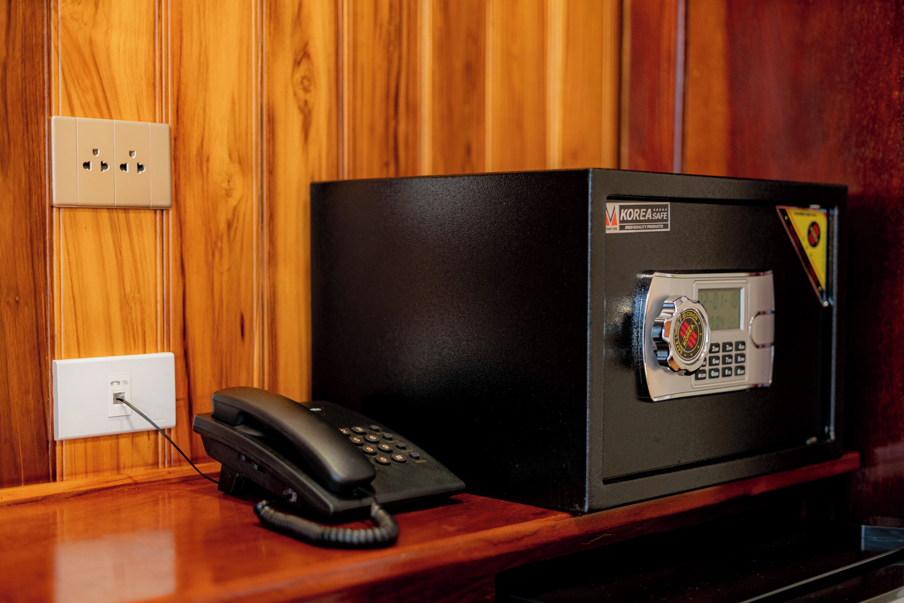 A safe with a keypad and a card reader, a telephone, and a power outlet on a wooden desk.