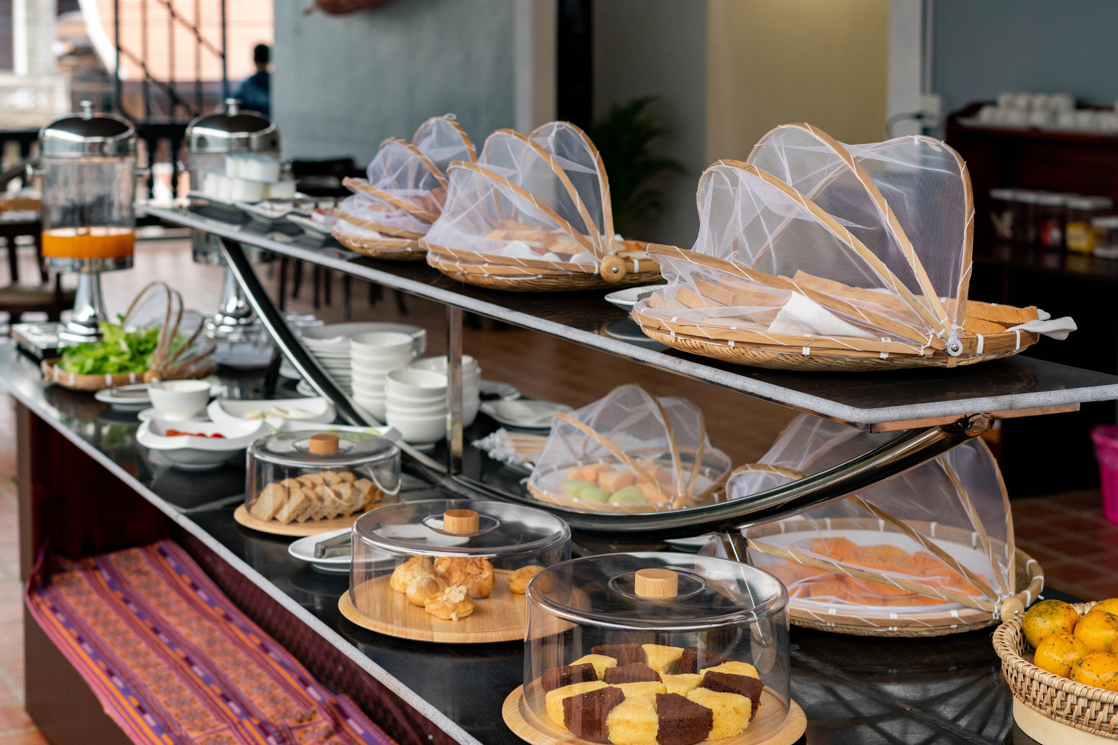 Een buffet met diverse soorten eten, waaronder brood, gebak en fruit, gepresenteerd op een toonbank met een decoratieve bank.
