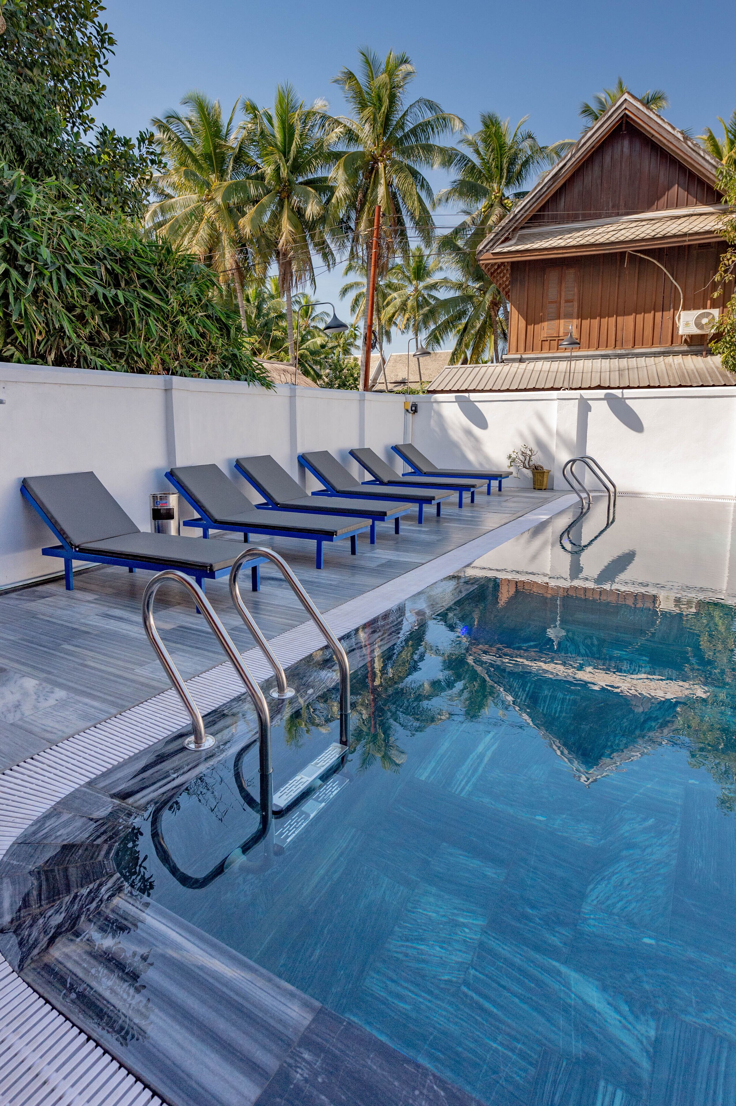 A swimming pool with lounge chairs, a wooden building, and palm trees.