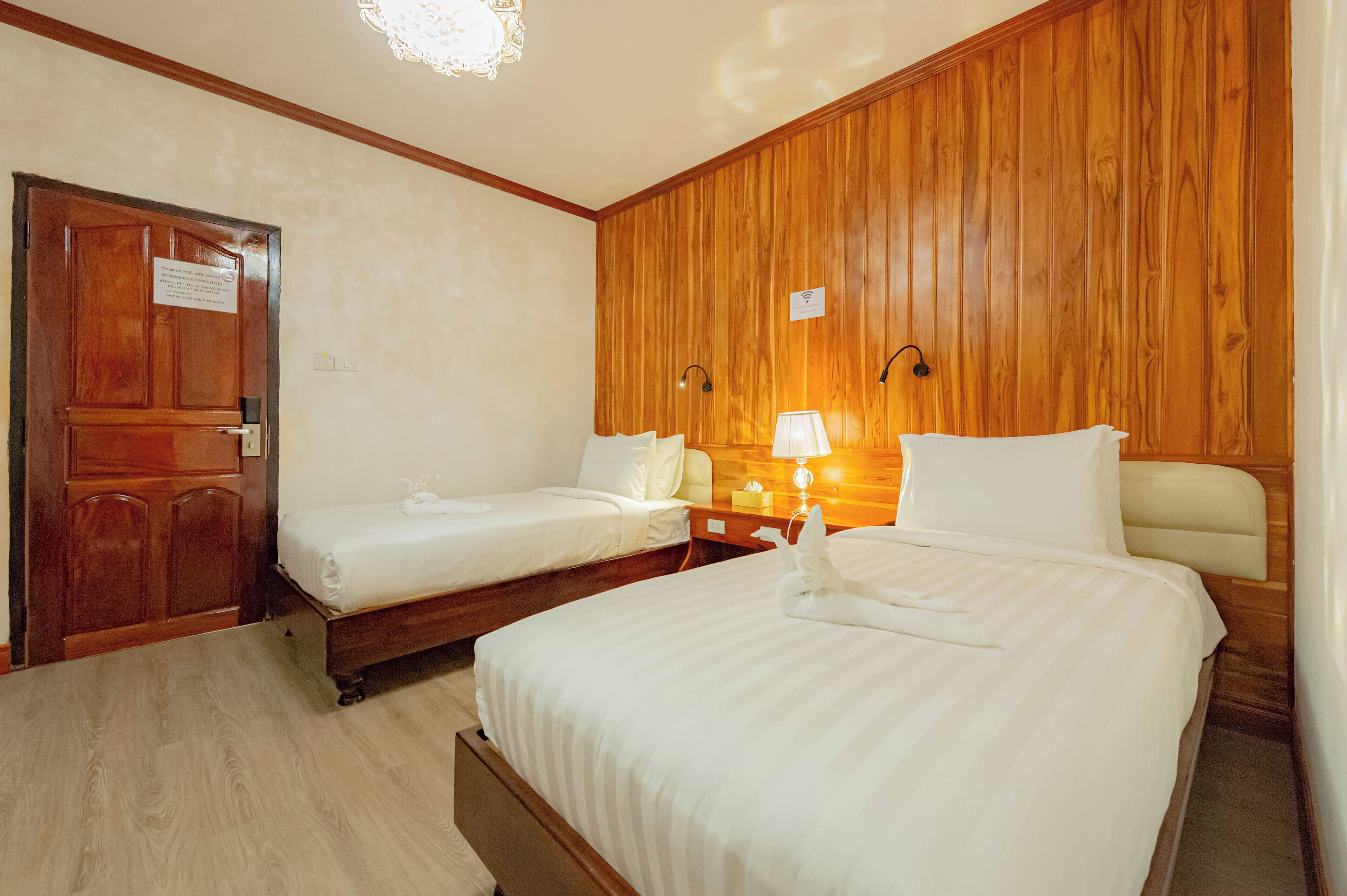 Ein Hotelzimmer mit zwei Einzelbetten, Holzwandverkleidung, einer Holztür und einem Nachttisch mit Lampe.