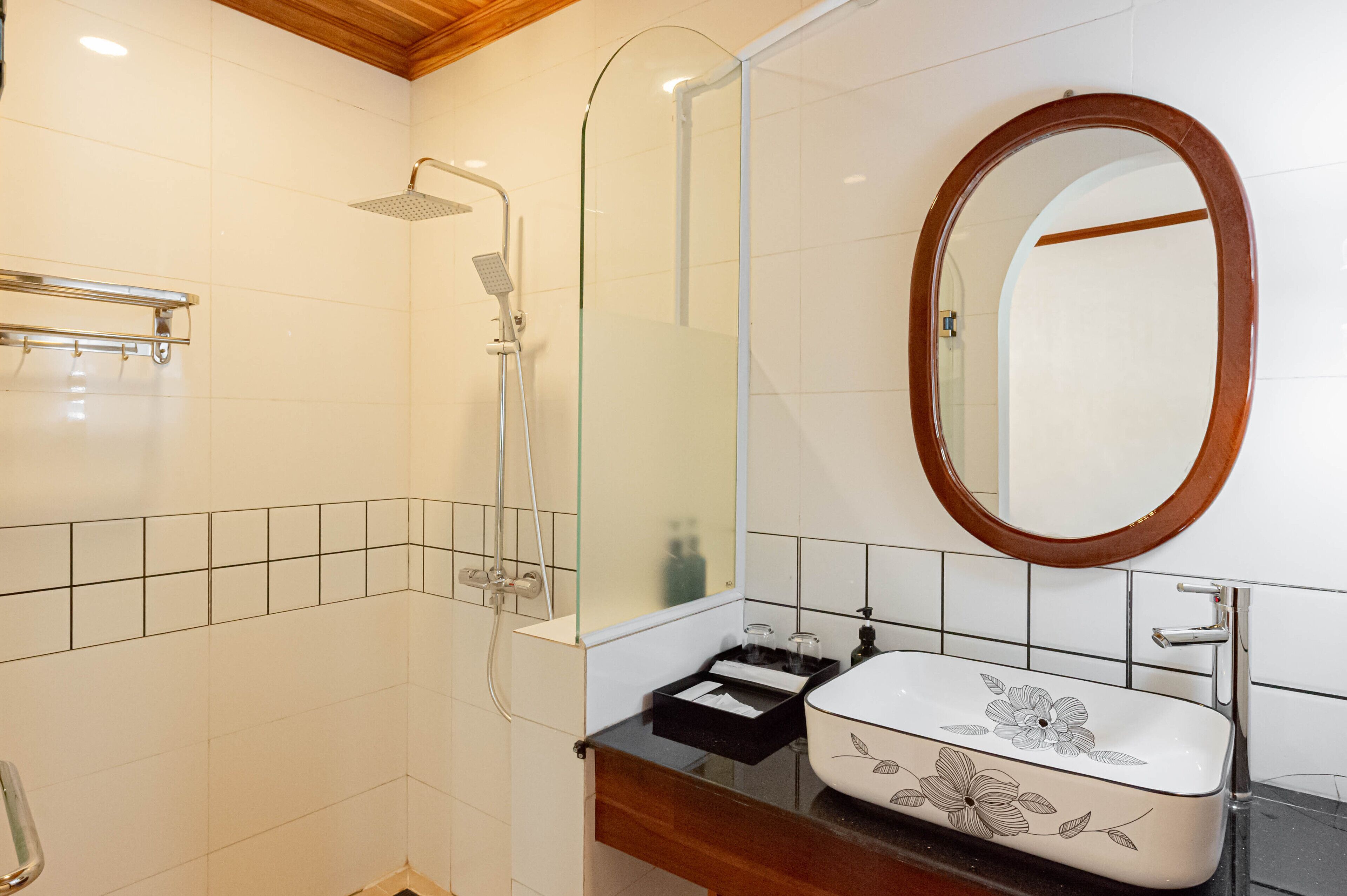 Une salle de bain avec une douche, un lavabo orné de motifs floraux, un meuble-lavabo en bois et un miroir avec un cadre en bois.