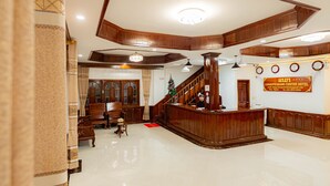 Un vestíbulo de hotel con un mostrador de recepción de madera, una escalera y un candelabro.