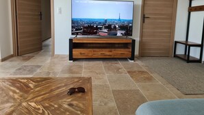A living room with a flat-screen TV on a wooden stand, a coffee table, and a door on the left. - Villa Indépendante - Piscine Privée - Clim - Vue Exceptionnelle (Orgnac l'Aven)
