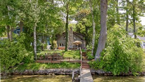 Une jetée en bois menant à une maison entourée d’une végétation luxuriante et d’arbres.