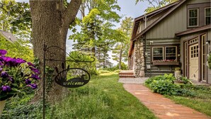Un sentier en bois mène à une maison en pierre sur laquelle est accrochée une pancarte indiquant « Bienvenue ».