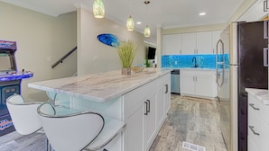 Moderni keittiö, jossa on valkoiset kaapit, marmorinen työtaso ja riippuvalaisimet.