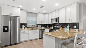 A modern kitchen with white cabinets, stainless steel appliances, granite countertops, and a breakfast bar. - Family Friendly! 3bd, 2BA Home! Close to Beach! HOT Tub! (Panama City Beach)