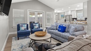 A spacious living area with a ceiling fan, a kitchen in the background, and a large window with blinds. - Family Friendly! 3bd, 2BA Home! Close to Beach! HOT Tub! (Panama City Beach)