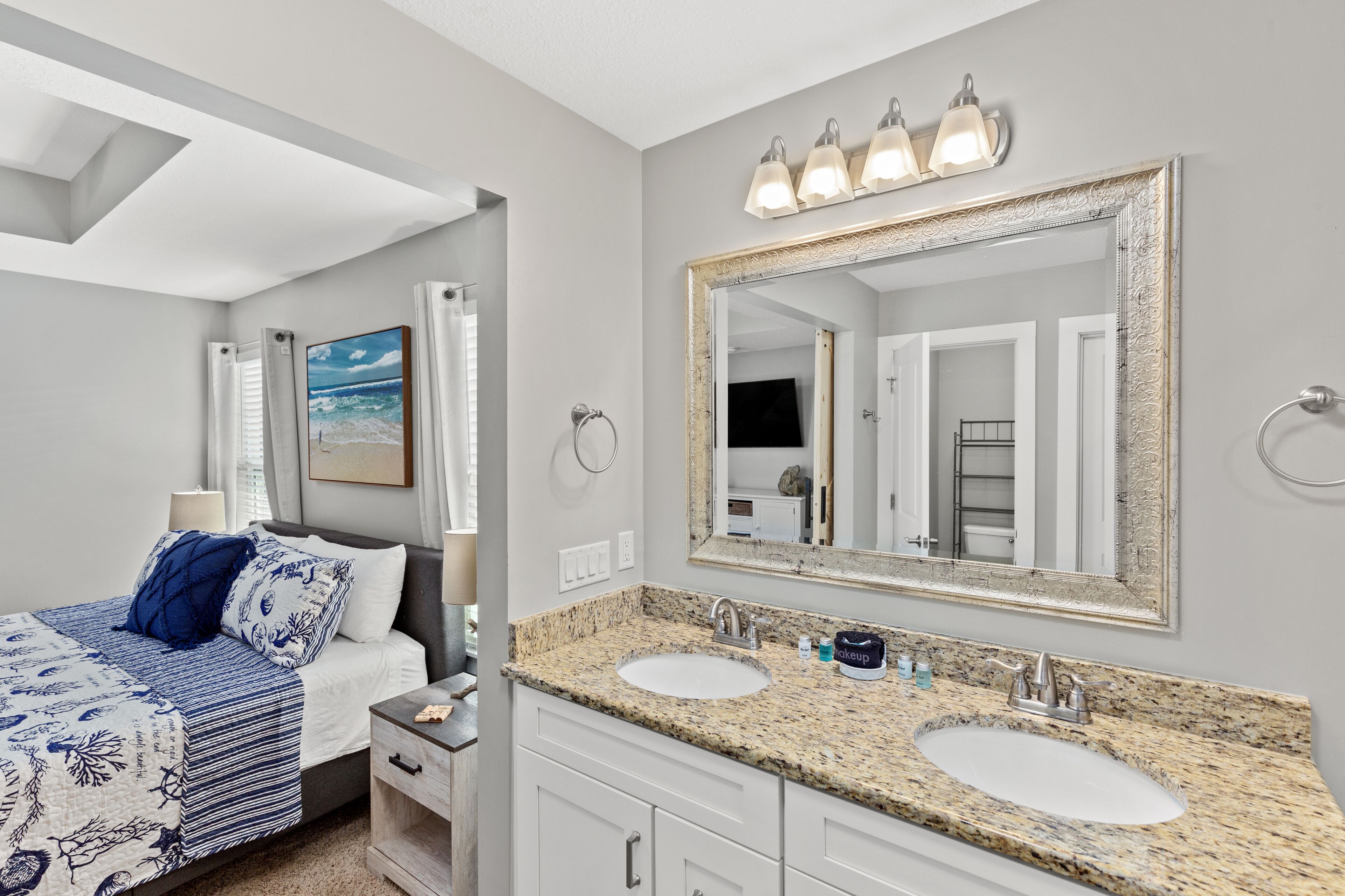 A bedroom with a bed, a nightstand, a double sink vanity, and a large mirror.
