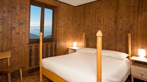 A wooden-paneled room with a four-poster bed, a window with a view, and a small desk with a chair. - Vacation Home Myrtle Bielmonte (piatto)
