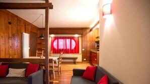 A cozy living room with wooden walls, a dining area with a red curtain, and a kitchen area with wooden cabinets. - Vacation Home Myrtle Bielmonte (piatto)