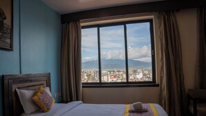 Een hotelkamer met een groot raam, een bed met een geborduurd beddegoed, een stoel en uitzicht op een stadsgezicht.