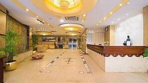 Een ruime lobby met een receptiebalie, een zithoek en decoratieve verlichting.