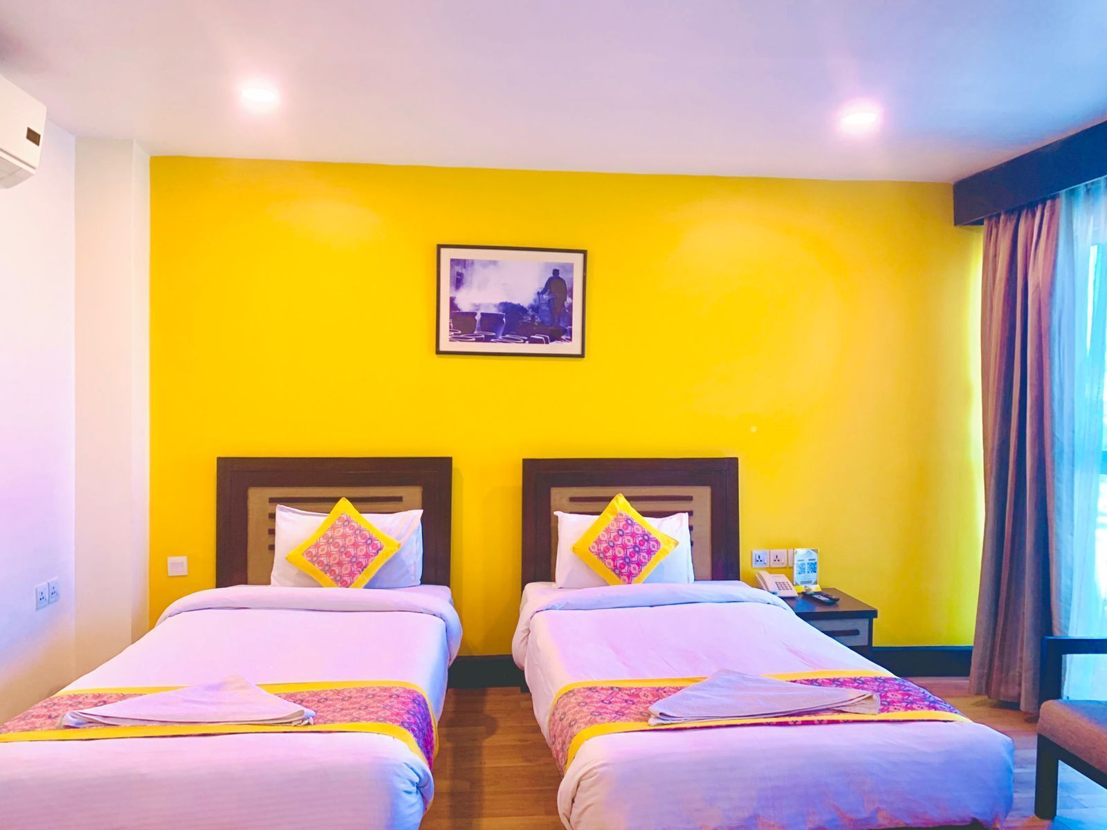 A hotel room with two beds, a small bedside table with a phone, and a picture on the wall.