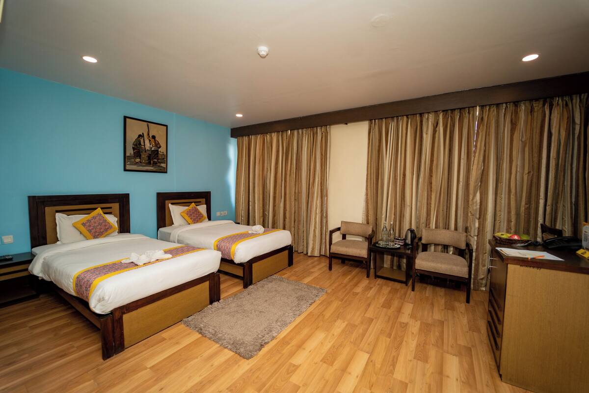 A hotel room with two beds, a desk, a chair, and a large window with curtains.