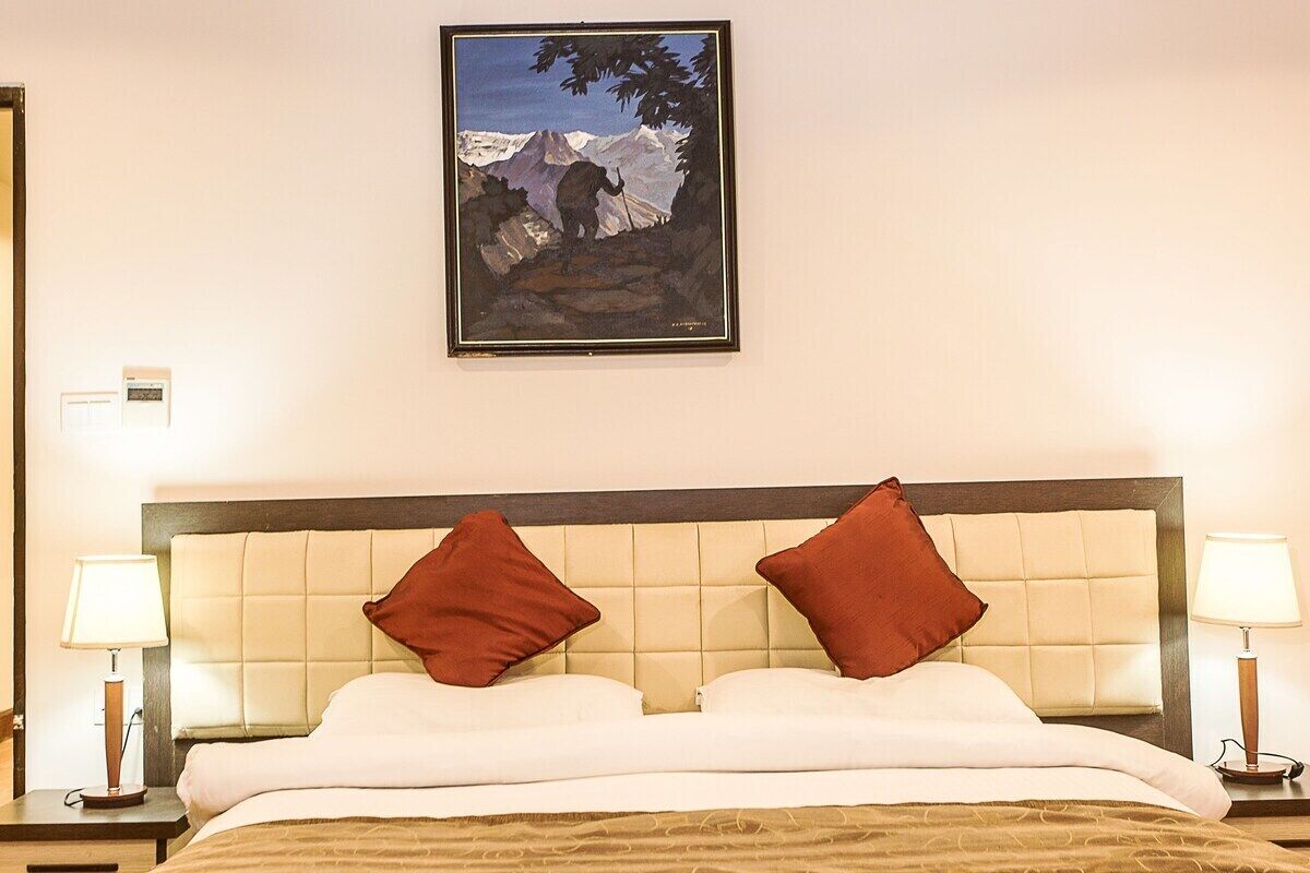 Habitación de hotel con cama, dos almohadas, cabecero, dos lámparas de noche y un cuadro en la pared.