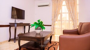 A living room with a sofa, a coffee table with a plant, a TV on a stand, and an air conditioning unit. - Dees Hotels (Lagos)