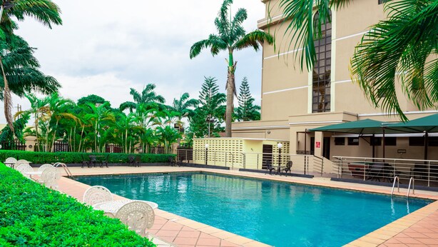 A swimming pool surrounded by palm trees and a building with a beige facade. - Dees Hotels (Lagos)