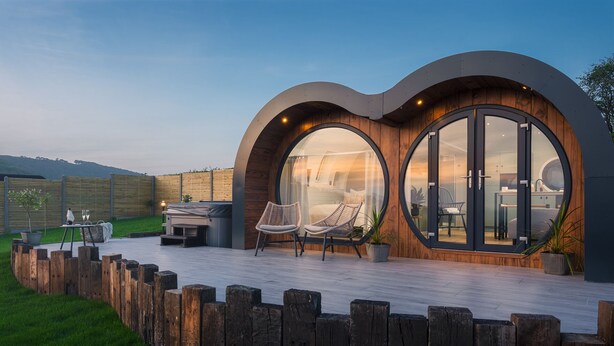 Una casa moderna con amplios ventanales circulares, una terraza de madera y mobiliario exterior.