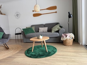 A modern living room with a grey sofa, a round wooden table, a green rug, and a wall-mounted lamp.