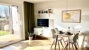 Uma sala de estar moderna com televisão, mesa de jantar, cadeiras e uma grande janela.
