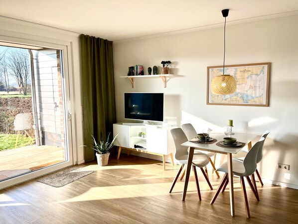 A modern living room with a TV, dining table, chairs, and a large window.