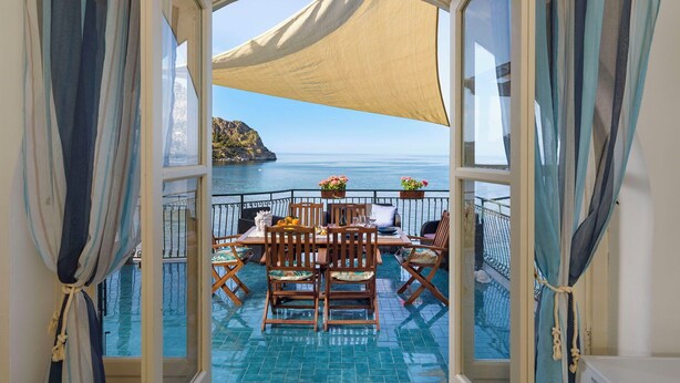 Een balkon met een tafel en stoelen, zeezicht en een groot zonnescherm.