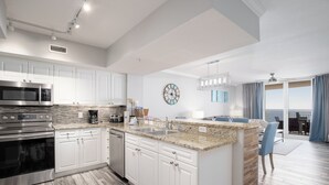 A modern kitchen with white cabinets, granite countertops, stainless steel appliances, and a large island with a sink.