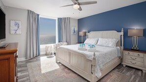 A bedroom with a bed, nightstands, a ceiling fan, and a view of the ocean.