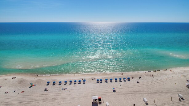 A beach with rows of umbrellas and beach chairs, a lifeguard tower, and the ocean in the background.