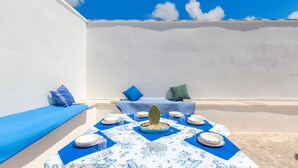 A sunlit outdoor dining area with a table set for four, surrounded by blue cushions and a cactus centerpiece. - 3315 Villetta Carmela by Barbarhouse (Alliste)