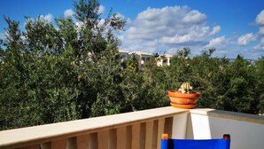 A balcony with a wooden table and blue chairs, a potted plant, and a view of greenery and buildings. - Escape and Relax Apartment (Mandria)